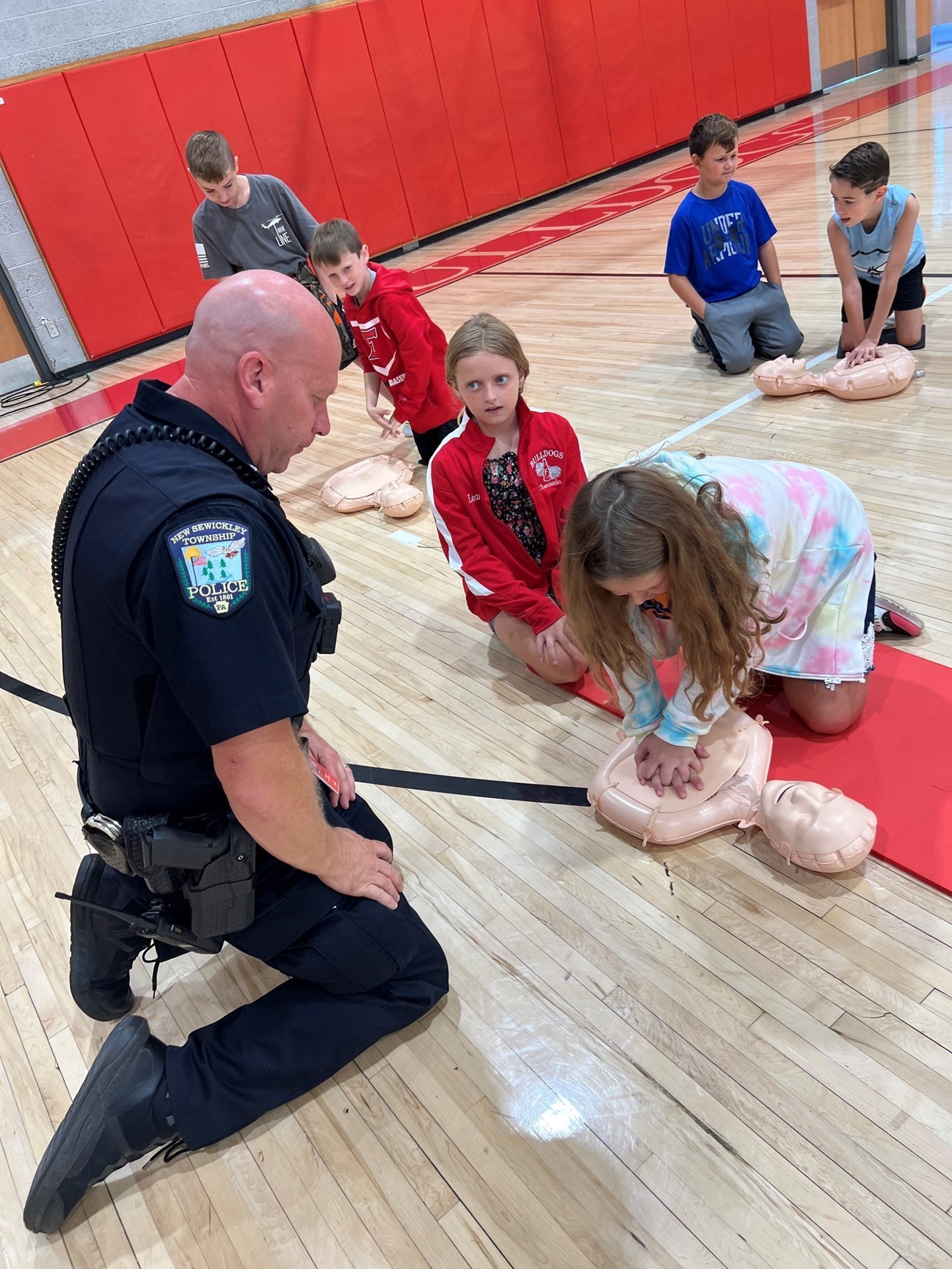 Police office in a wooden gym with red walls. Kids kneeling down.