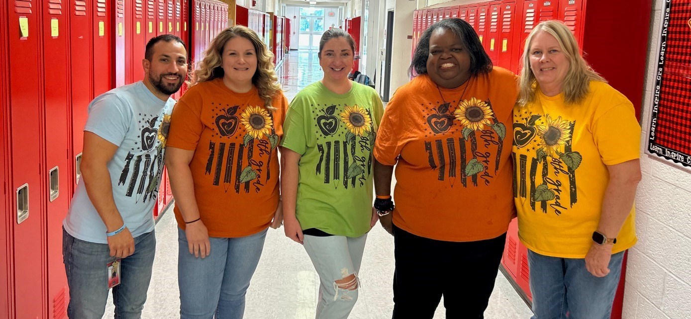 Hallway with red lockers and teachers in blue, orange, green and yellow t-shires with writing and sunflowers on it.
