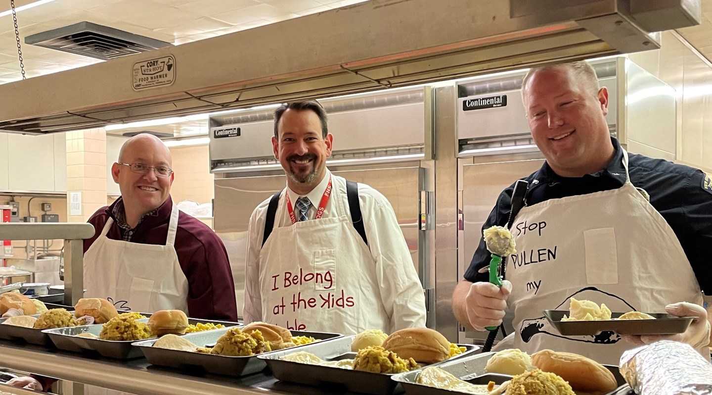 School Cafe line.  3 men serving lunches.